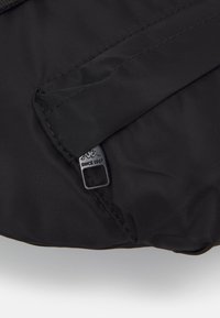 Fekete nylon táska textúrált felülettel, varrott zsebbel és fém márkajelzéssel. A dizájn egyszerű és funkcionális.