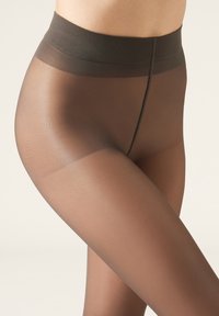 Transparent bruna strumpbyxor med en slät yta och ett brett elastiskt midjeband. Visade på en modells ben, vilket visar den åtsittande stilen.