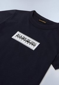 Camiseta de algodón azul marino con cuello redondo que presenta un logotipo rectangular blanco con el texto "NAPAPIJRI geographic" en una fuente en negrita.