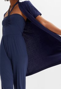 Mono azul marino con diseño sin tirantes, frente fruncido y pantalones de pierna ancha, combinado con un kimono de frente abierto a juego. Tejido suave.