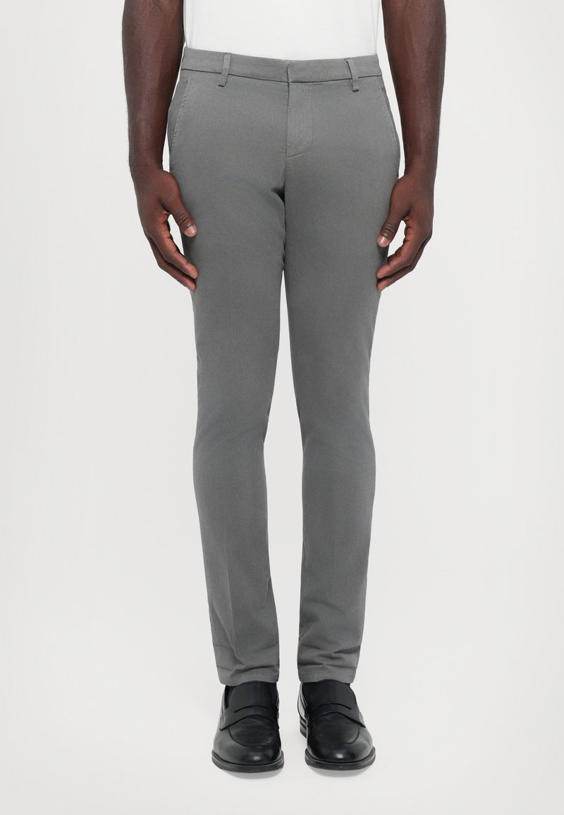 Pantaloni slim-fit grigi realizzati in tessuto liscio, dotati di tasche frontali e zip, abbinati a scarpe nere.