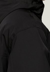 Czarna wodoodporna kurtka z wysokim kołnierzem, gładką fakturą i przeszyciami na ramionach dla zwiększenia trwałości.