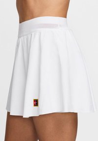 Witte sportrok met een textuur-elastische tailleband, uitlopende ontwerp en een klein multikleurig Nike-logo aan de zoom.