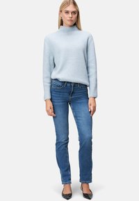 Helles blaues geripptes Sweatshirt mit hohem Kragen, kombiniert mit dunkelblaue, figurschmeichelnden Jeans und schwarzen spitzen Absätzen mit Nieten.