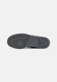 Sola de sapatilha preta com um design de borracha texturizada, apresentando um logótipo e um padrão de piso para tração. Design oval plano e largo.