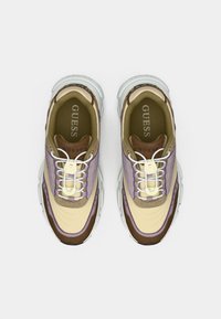 Αθλητικά παπούτσια με συνδυασμό κρεμ μπεζ, καφέ και μοβ υλικών· υφή στο πάνω μέρος, λευκή μεσαία σόλα και εμφανείς κορδόνια.