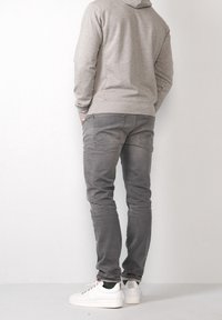 Sudadera gris con vista trasera completa, combinada con jeans grises y zapatillas blancas. La tela parece suave; los jeans tienen bolsillos traseros.