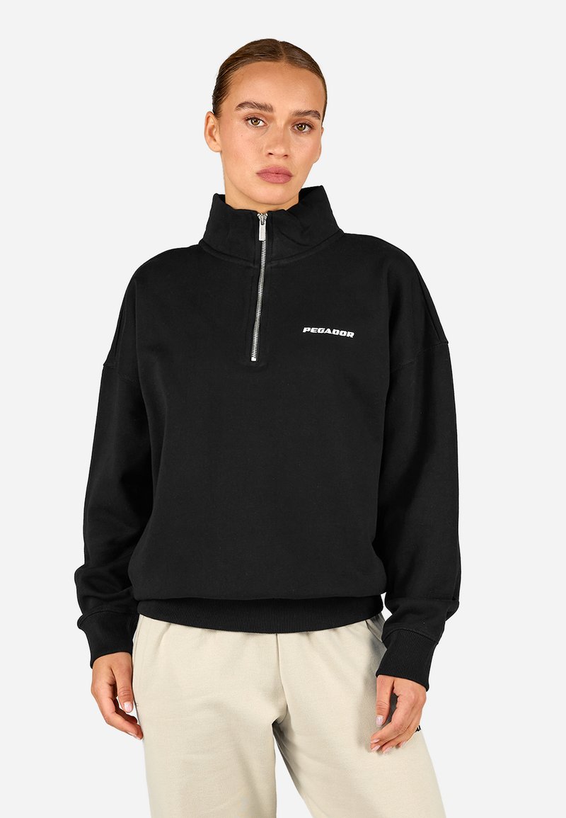 Melns puloveris ar augstu apkakli, pusī zips priekšā, ribotas aproces un apakša, ar balto "PEGADOR" logo uz krūšu daļas.