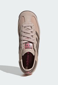 Béžová semišová teniska s texturovanými doplňky, třemi tmavými pruhy a růžovým logem na jazyku a stélce. Šněrování a polstrovaný límec.