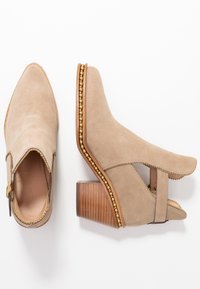Beżowe zamszowe botki do kostki z drewnianymi obcasami, złotą bead trim wzdłuż podeszwy i krawędzi, wycięciami po bokach oraz stylem wsuwanym.