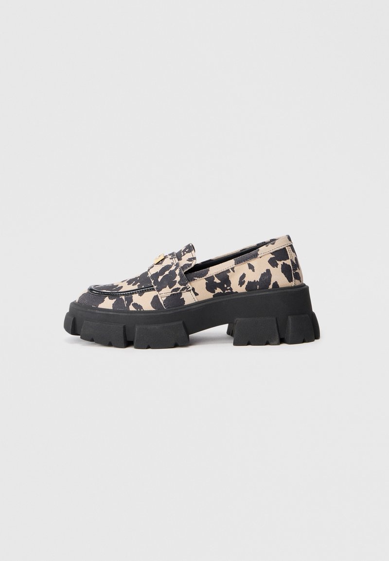 Mocassin à semelle épaisse avec dessus imprimé animal beige et noir et détail métal doré sur le coup de pied, sur fond gris clair.