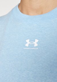 Pilkiai mėlynas medvilninis marškinėliai su apvalia iškirpte ir švelnia tekstūra. Yra baltas "Under Armour" logotipas ant krūtinės.