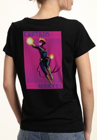 Camiseta de algodón negra con un gráfico colorido de Captain Marvel en una pose dinámica, con brillantes acentos amarillos y rosas sobre un fondo de puntos.