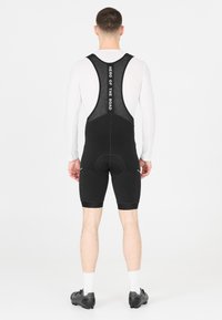 Shorts de vélo noirs avec bretelles en mesh, rembourrage au niveau du siège et éléments réfléchissants. Conçus pour le confort lors des activités de cyclisme.