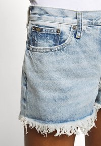 Ljust blå denimshorts med fransad fåll, med en klassisk femfickdesign och en liten logotagg nära frampocket.