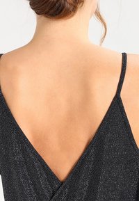 Svart klänning med en djup V-backdesign. Tillverkad av texturerad tyg, med subtila metalltrådar för en skimrande effekt. Tynda remmar.