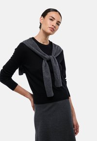 Pull en maille noire avec un cache-cœur en maille grise noué au niveau du col, doté de manches longues et d'une taille cintrée, associé à une jupe gris foncé.