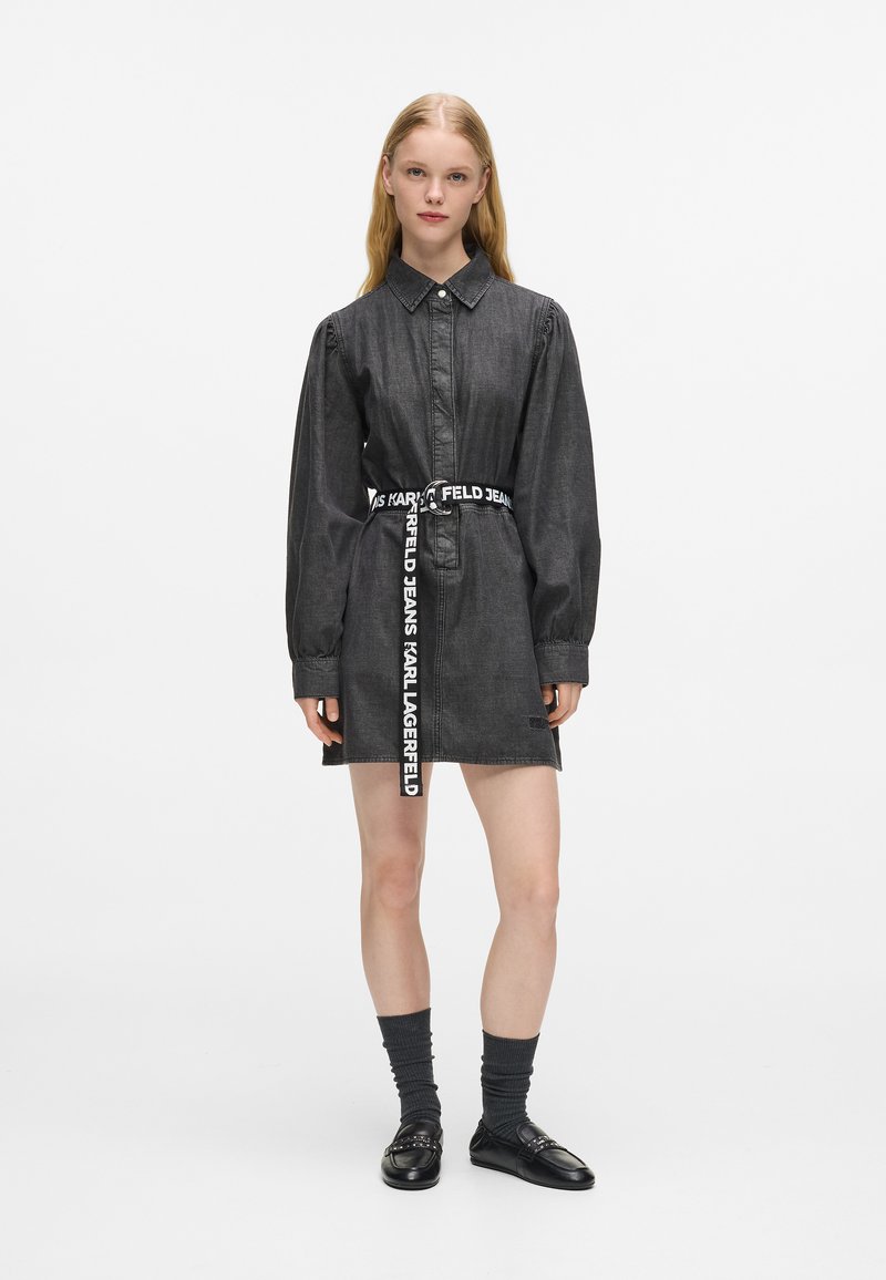Czarna sukienka koszulowa z denimu z długimi rękawami, z przodu zapinana na guziki oraz z kontrastującym paskiem z logo. Gładka tekstura i dopasowany krój, długość do kolan.
