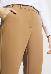 Bruna byxor i mjukt tyg, med rak bendesign, sidofickor och platt framstycke med en subtil veckdetalj.