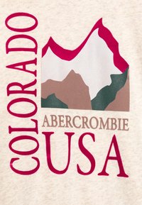 Béžové tričko z grafického materiálu s designem hor v růžové, zelené a hnědé barvě, s textem "COLORADO" a "ABERCROMBIE USA".