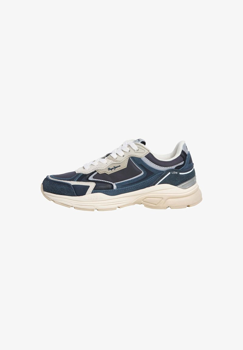 Zapatilla deportiva en azul marino y beige, que presenta una mezcla de materiales, con detalles de malla y ante, cordones blancos y una suela texturizada con detalles del logo.