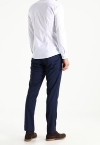 Witte langemouwen shirt met een getailleerd ontwerp, gecombineerd met marineblauwe broek. Bruine suède laarzen maken de outfit compleet voor een verzorgd uiterlijk.