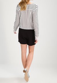 Raidallinen pitkähihaine pusero mustavalkoisena, yhdistettynä mustiin shortseihin. Hihoissa on pitsikoristeita ja hopeiset korkeat sandaalit.