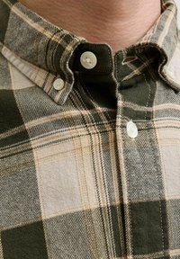 Camisa de cuadros verde y beige con cuello. Presenta botones blancos y una textura de tela con un patrón tejido. Vista detallada.