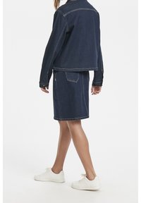 Mörk denimmantel som är matchad med en kjol, med kontrastsömmar, en figursydd design och vita sneakers.