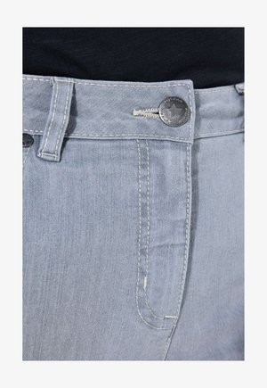 Primo piano della vita di jeans denim grigio chiaro, con bottone di metallo a forma di stella, passante per cintura e dettaglio della tasca cucita su sfondo di tessuto nero.