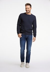 Laivastonsininen neulottu pooloneule, slim fit -siniset farkut ja valkoiset tennarit. Kangas on teksturoitua; neuleessa on resorit hihansuissa ja helmassa.