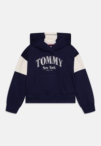 Marinegenser med hvite aksentermede, som har "TOMMY New York" i sølvfarge. Inkluderer en frontlomme og ribbestrikkede mansjetter.