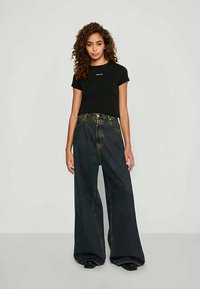 T-shirt preta de algodão com mangas curtas e logótipo branco, combinada com calças de ganga escuras, cintura subida e pernas largas. Textura suave, design minimalista.