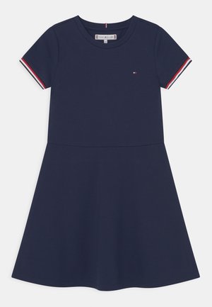Granatowa sukienka z krótkim rękawem, z czerwono-biało-granatowym paskiem na rękawach, okrągłym dekoltem i małym logo na piersi.