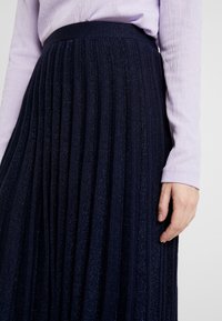 Marinblå plisserad kjol med en texturerad yta, som har fina metalltrådar. Matchad med en ljuslila ribbad långärmad topp.