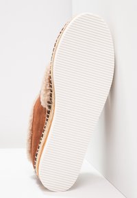 Brown suede slipper with a fluffy beige lining. White rubber sole with textured grooves. Side stitching visible along the edges.