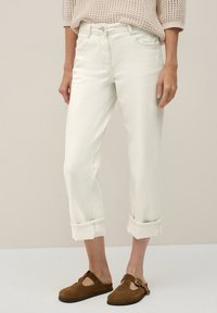 Avklippta vita denimjeans med upprullade fickor, fem fickor och dragkedja. Bärs med bruna mockaskor utan snörning. Texturerad stickad topp.