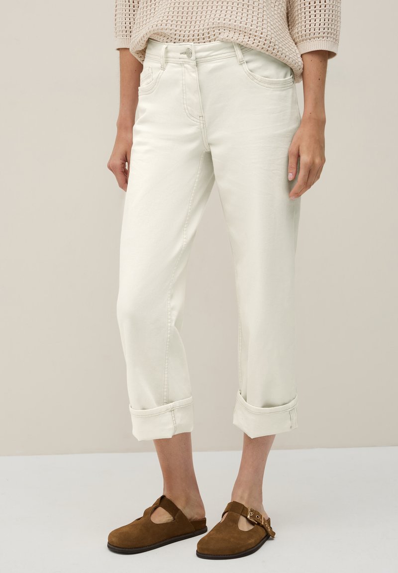 Avklippta vita denimjeans med upprullade fickor, fem fickor och dragkedja. Bärs med bruna mockaskor utan snörning. Texturerad stickad topp.