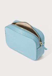 Geantă cosmetică din piele de culoare albastru deschis, cu un finisaj texturat, fermoar aurit și un mânere mic pe lateral. Include numele brandului pe față.