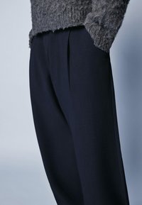 Granatowe spodnie o gładkiej fakturze i plisowanym przodzie. Dobranie z dzianinowym, szarym, puszystym swetrem dla kontrastu.