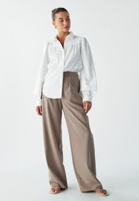Bílá košile s krátkými rukávy a širokými nohavicemi v béžové barvě. Outfit se vyznačuje hladkými texturami a uvolněnými liniemi.