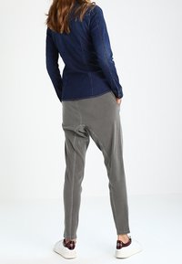 Dunkelblaues Jeansjacke in taillierter Form. Hellgraue, schmal zulaufende Hose mit tiefem Schritt, kombiniert mit weißen Sneakers.