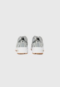 Graue Sportschuhe verfügen über ein Mesh-Design, gepolsterte Kragen und eine weiße Zwischensohle mit einer Gummisohle, die eine einzigartige Rückform präsentieren.