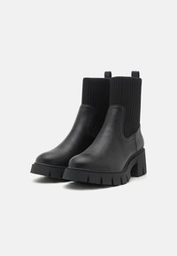 Black ankle boots with a leather foot and ribbed knit shaft. Features a block heel and textured sole with pronounced grooves.