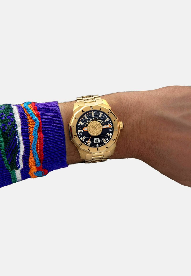 Gouden horloge met een blauwe wijzerplaat, grote indexen en 'CARLO COLUCCI' branding. Voorzien van een geprofileerde armband en automatische beweging.