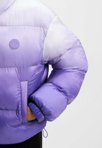 Polstret jakke i gradient lavendel, med et rundt logo på brystet, elastiske cuffs og en frontlomme med en sømdetalje.