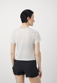 Hvit kortermet treningstopp laget av lett, pustende stoff. Har en avrundet hals og en avslappet passform, kombinert med sorte shorts.