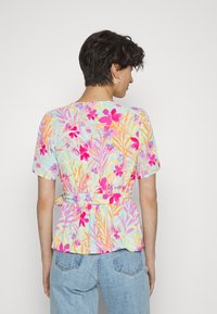 Blusa floral multicolorida com mangas curtas, apresentando flores rosas e laranjas em fundo azul claro, cintura ajustada e design peplum.