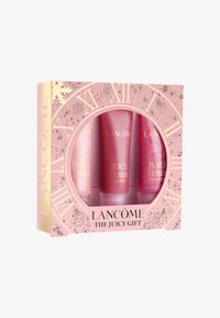 Kolme huulikiillon putkea, joissa on vaaleanpunaisia ja läpinäkyviä sävyjä sekä kultaisia yksityiskohtia, esitettynä koristeellisessa vaaleanpunaisessa laatikossa, jossa on kellosuunnittelu.