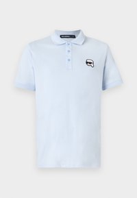 Polo bleu clair à manches courtes avec trois boutons et un petit écusson logo noir et blanc représentant un visage avec des lunettes de soleil sur la poitrine.